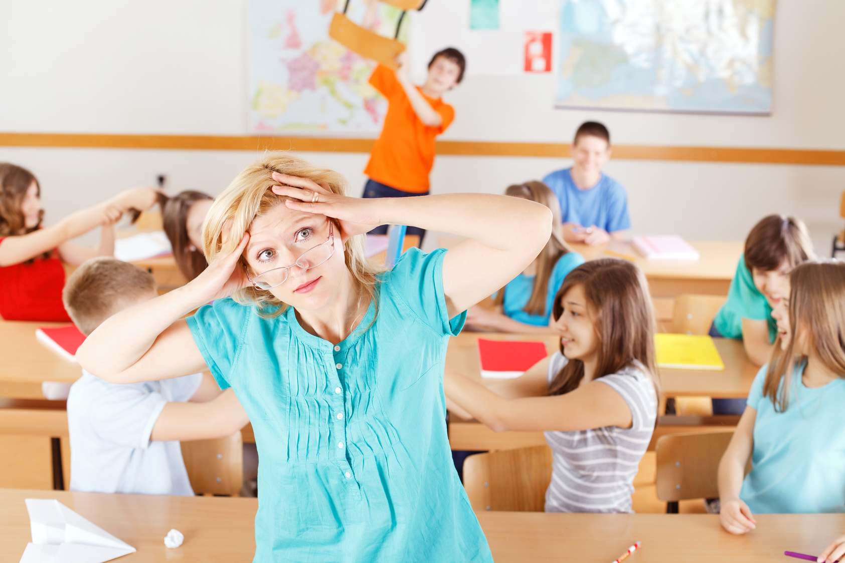 Frustrated teacher in classroom, pupils behind her behave bad.